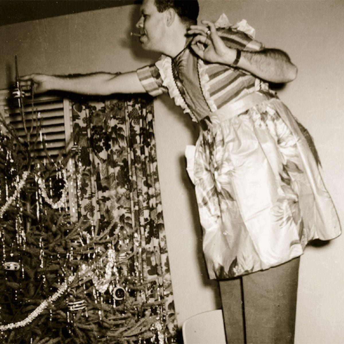 Man wearing a festive apron adding ornaments to a Christmas tree