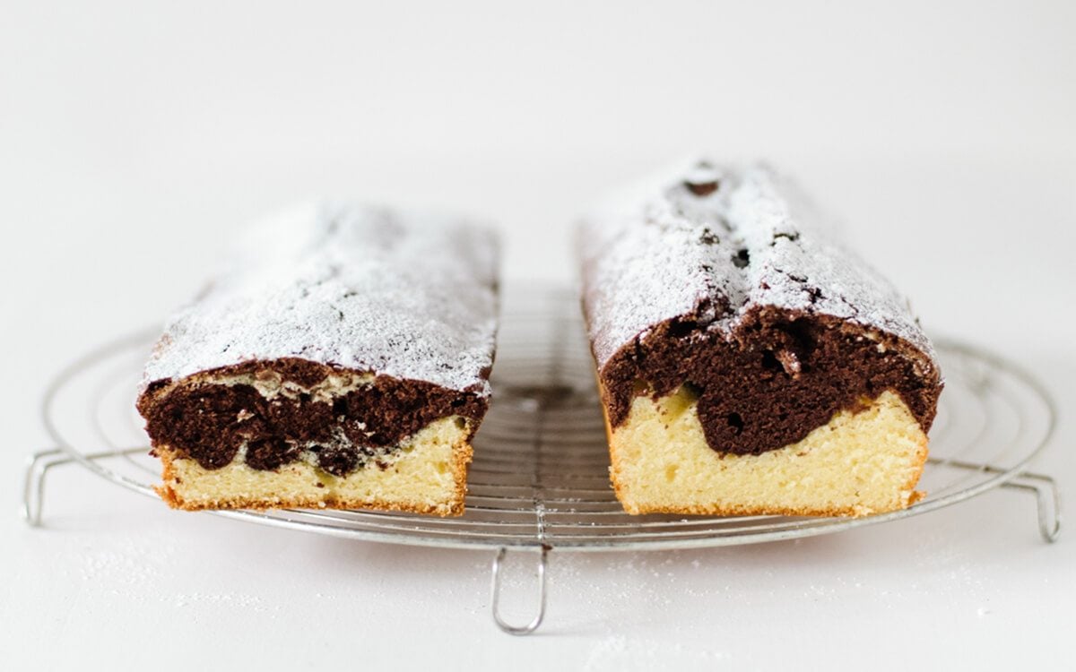 Two different vanilla chocolate marble cakes dusted with powdered sugar next two each other for a comparison to see baking mistakes or fails on cooling rack on white background