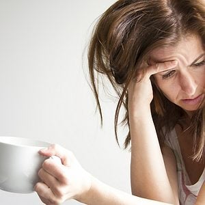 Tired and sad woman is sitting in the window seat with a cup in her hand. Depression concept