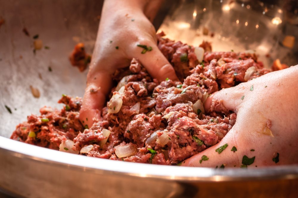 Pair of hand mixing raw ground beef mixture preparing to make fresh gourmet hamburgers