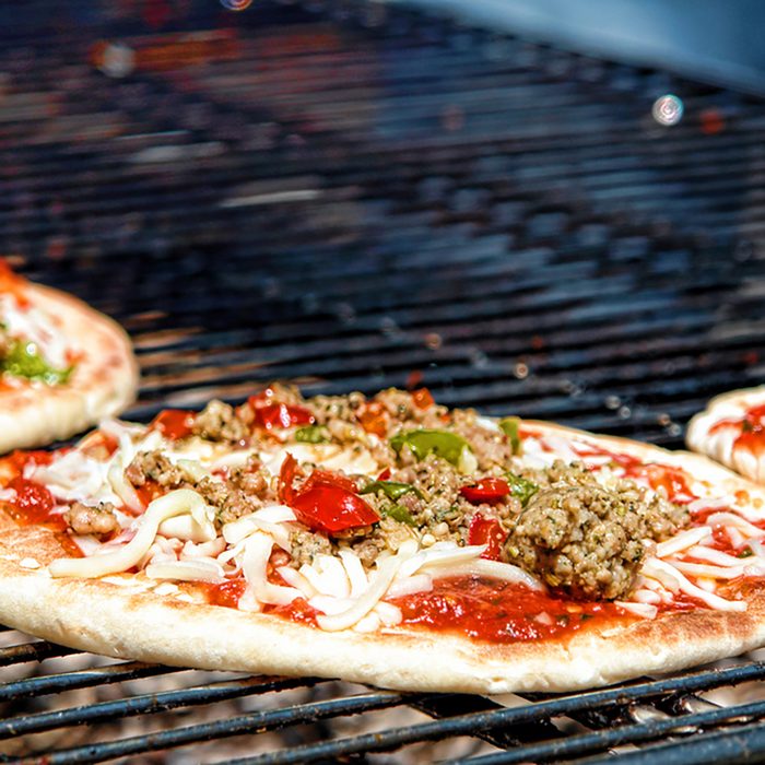 Pizza pie with sausage and peppers cooking on a charcoal grill in an Italian pizzeria
