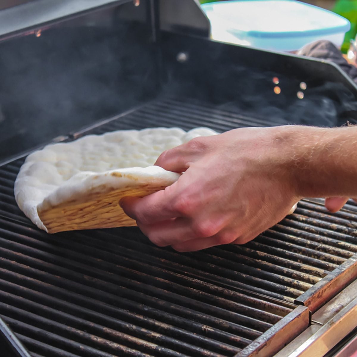 Hand flipping flatbread cooking on outside electric grill showing browned bottom and top not yet cooked