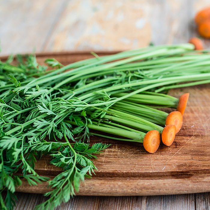Green tops of carrots on wooden board.