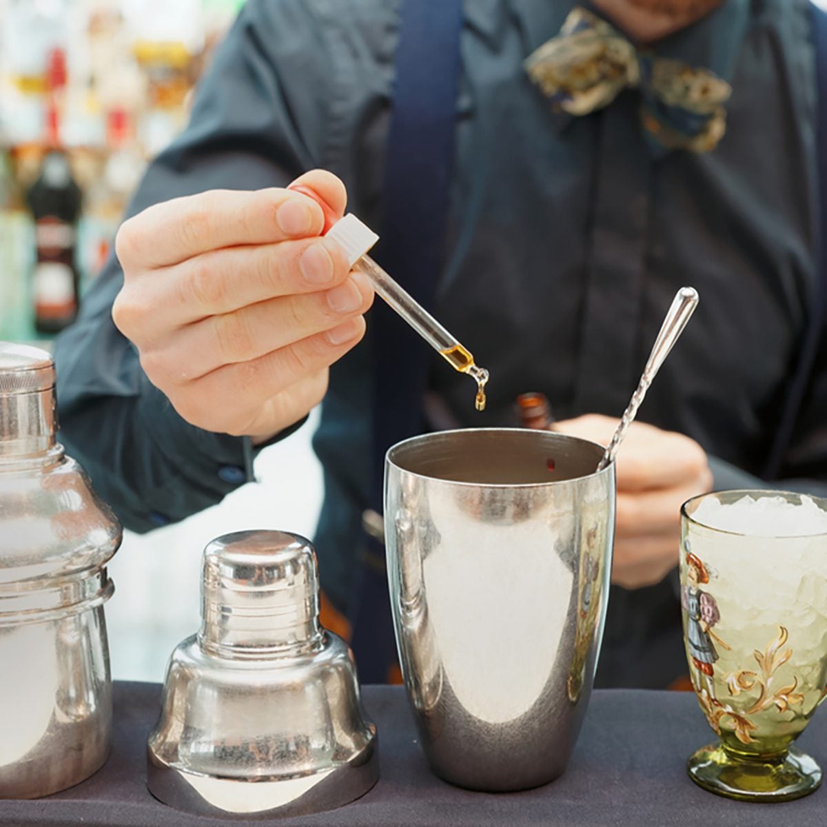 Bartender is making cocktail at bar counter, adding some bitter in the shaker