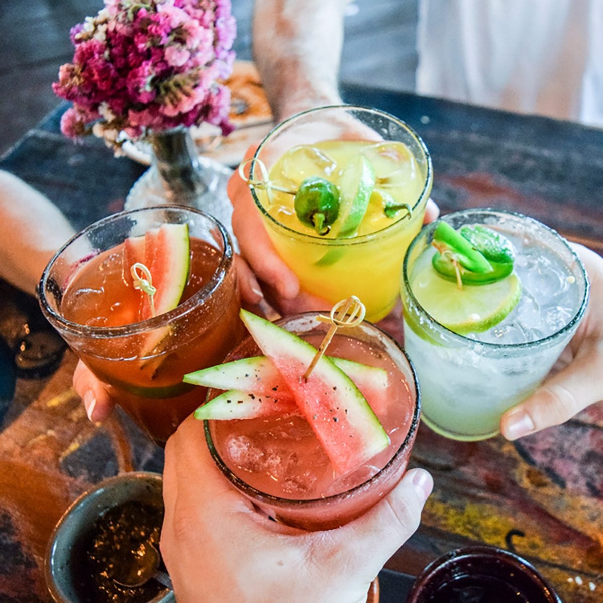 Friends toasting, saying cheers holding tropical blended fruit margaritas.