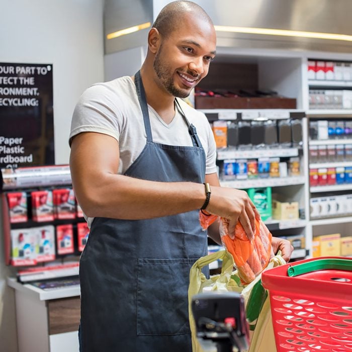 Smiling salesman putting vegetables in bag for customer after billing