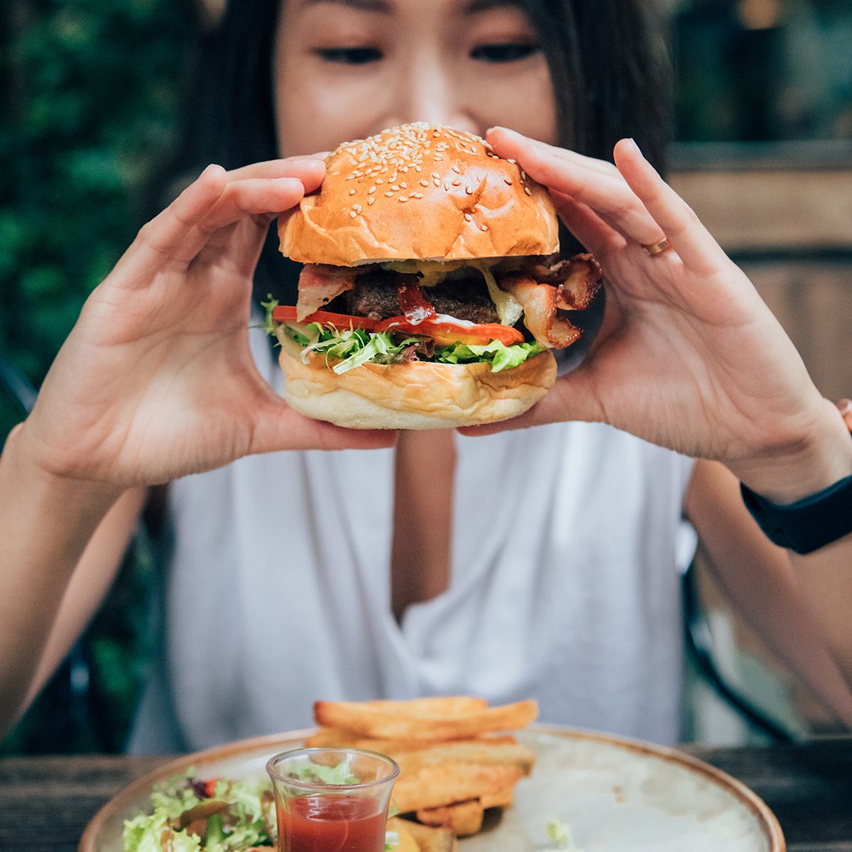 Young Woman Eating Burger At Restaurant With Outdoor Seating