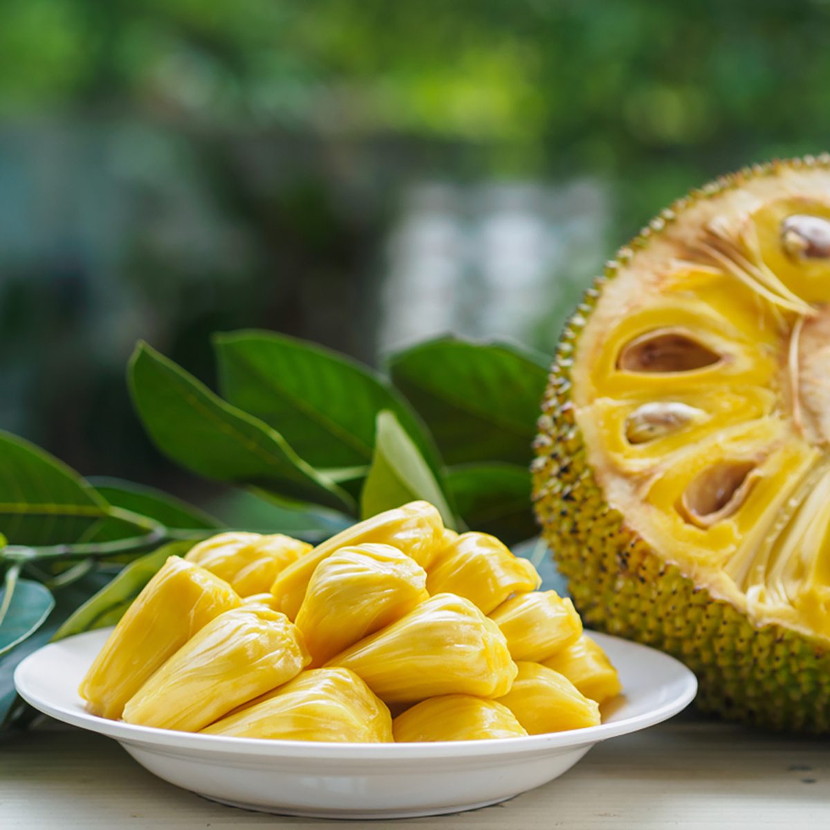 Fresh Jackfruit in white dish, half of jack fruit and jackfruit leaf on wooden table