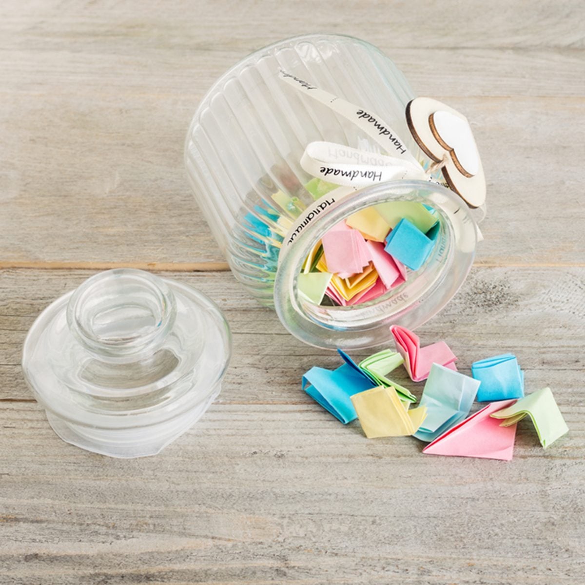 Glass jar with handmade wooden hearts decorations and ribbon filled with colorful pastel paper notes spilling over.; Shutterstock ID 696530689; Job (TFH, TOH, RD, BNB, CWM, CM): TOH