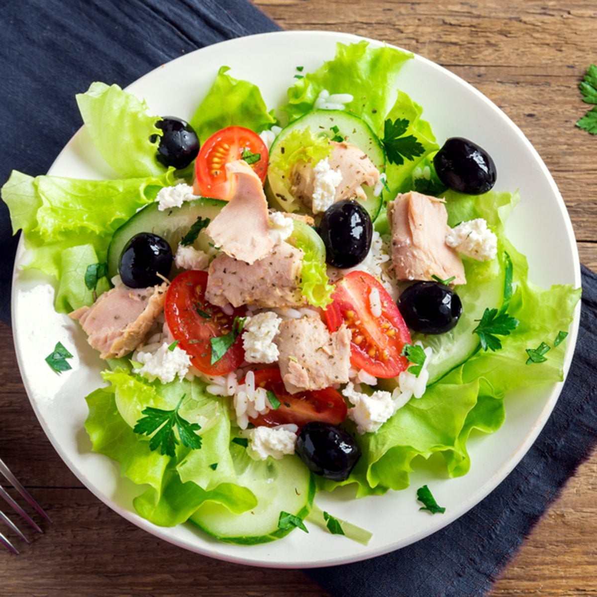 Tuna salad with tomatoes, black olives, rice, feta cheesse and greens on rustic wooden background with copy space