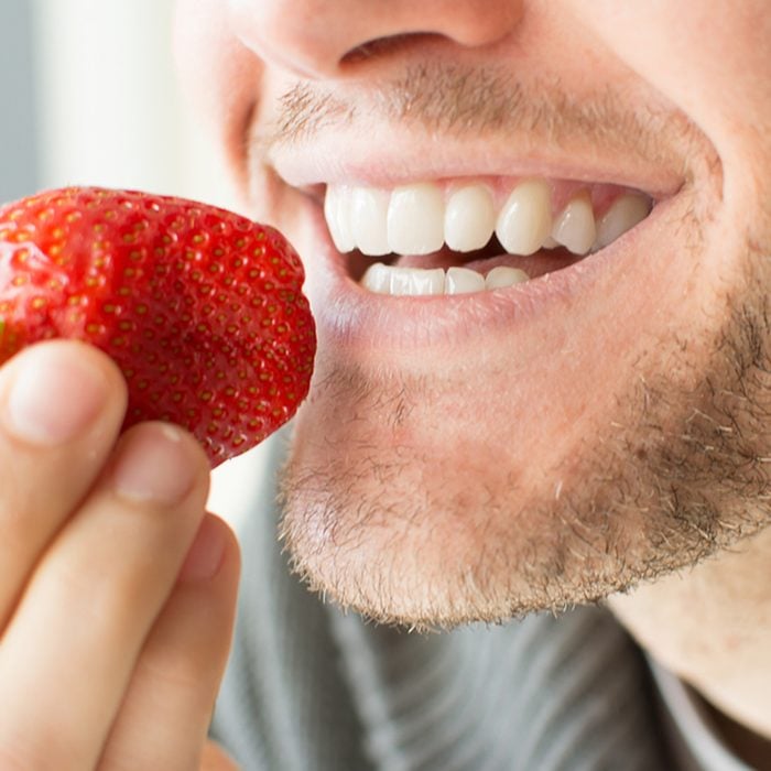 Young man holding a strawberry and smiling