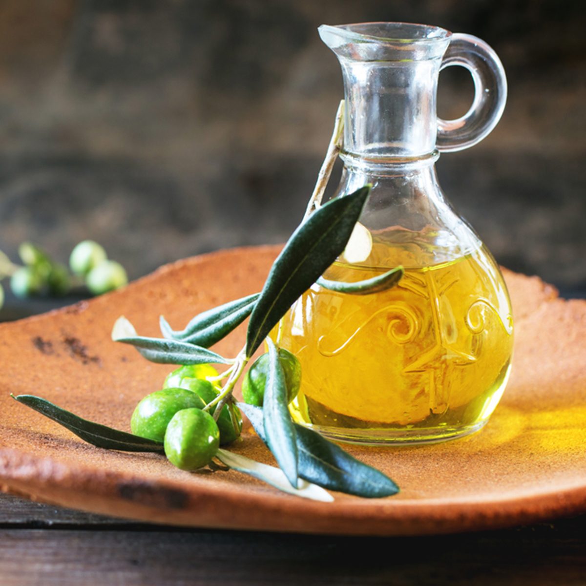 Bottle of olive oil with olive branch in handmade clay plate over wooden table.