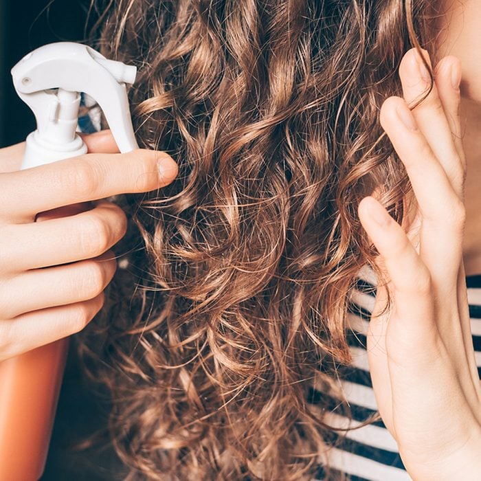 Woman applying spray on curly brown hair close-up