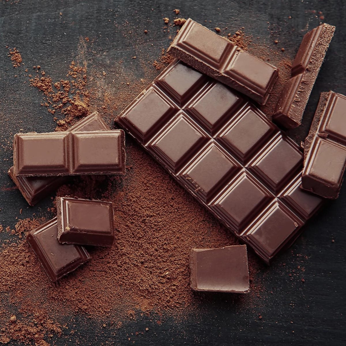 Broken chocolate pieces and cocoa powder on wooden background