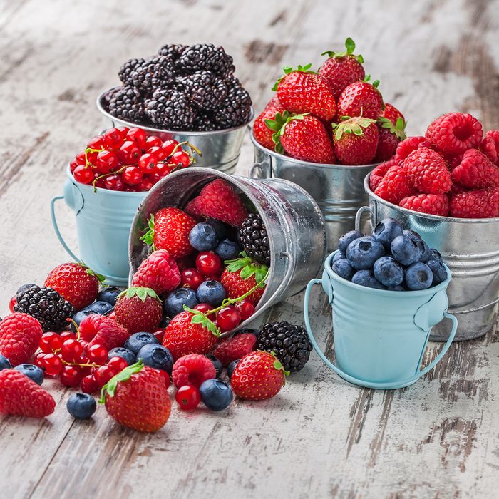 Berries mix blueberry, raspberry, red currant, strawberry, in five old tin cans spilled on white rustic wooden table in studio