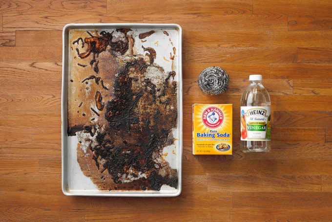 Dirty Baking Sheet next to box of baking soda, bottle of white vinegar, and steel wool on wood butcher block background