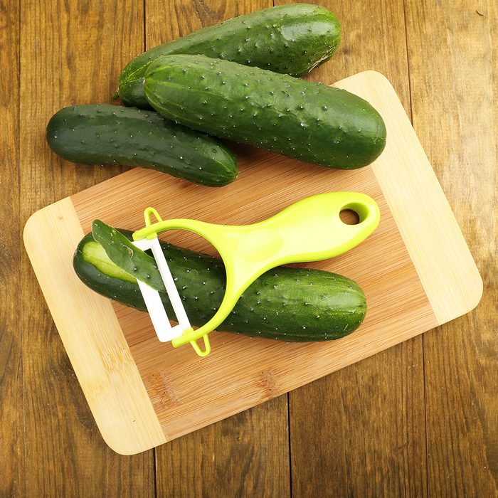 Peeler and cucumbers on wooden table