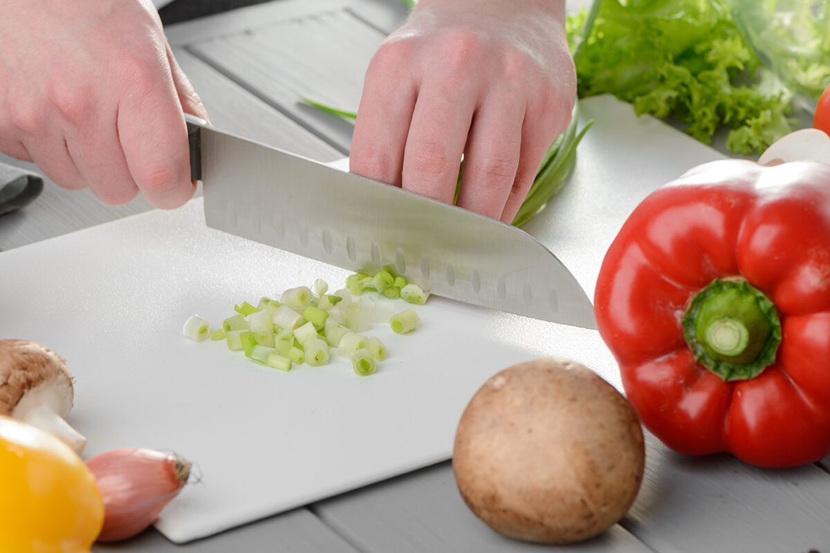 Chef cook chopping spring onions on a white board.