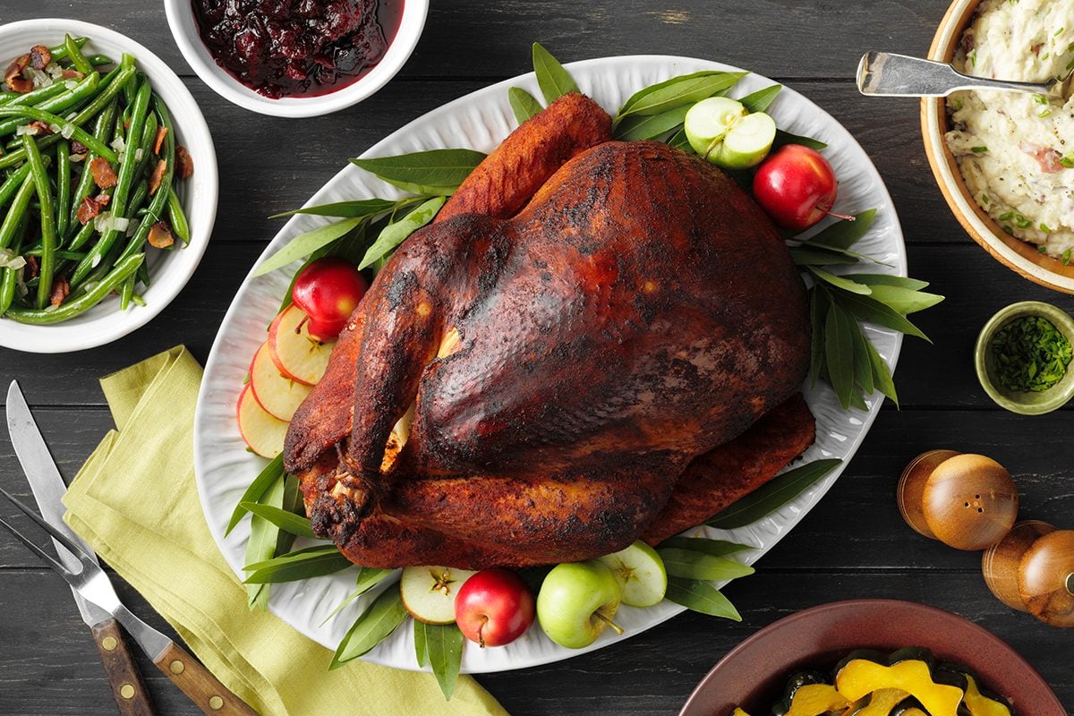 A smoked turkey on a platter arranged beautifully on a Thanksgiving table.