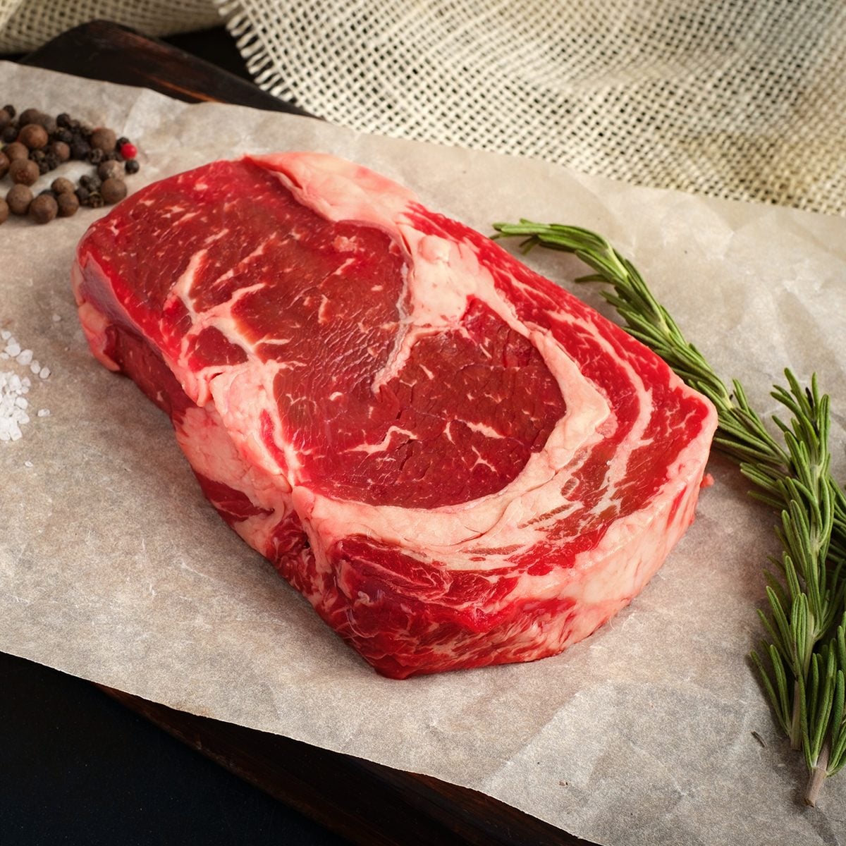 raw ribeye steak lying on Kraft paper around the pepper, salt, rosemary on a wooden Board