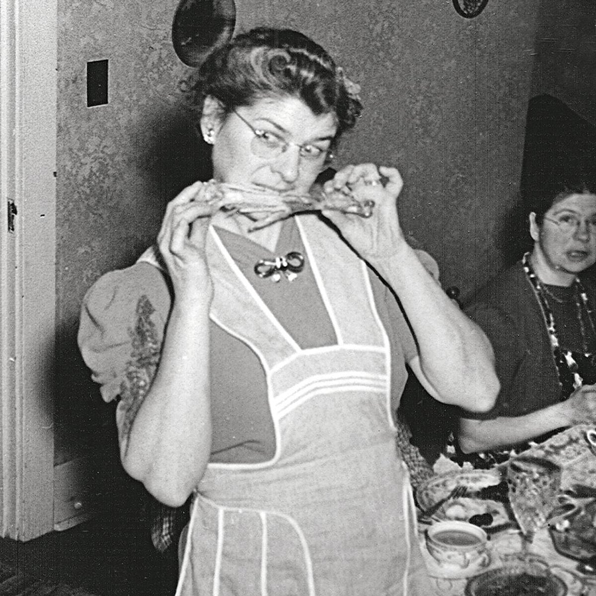 1930s woman jokingly biting a turkey leg while family looks on in confusion