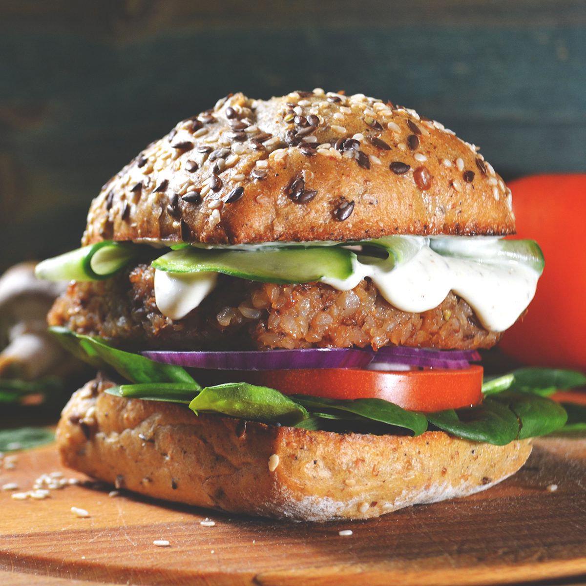 veggie, vegan burger with buckwheat, tomato, onion, vegan mayonnaise and spinach on a fresh bun with flax seeds and sesame, surrounded by spinach leaves, mushrooms, tomato, black pepper and spices.