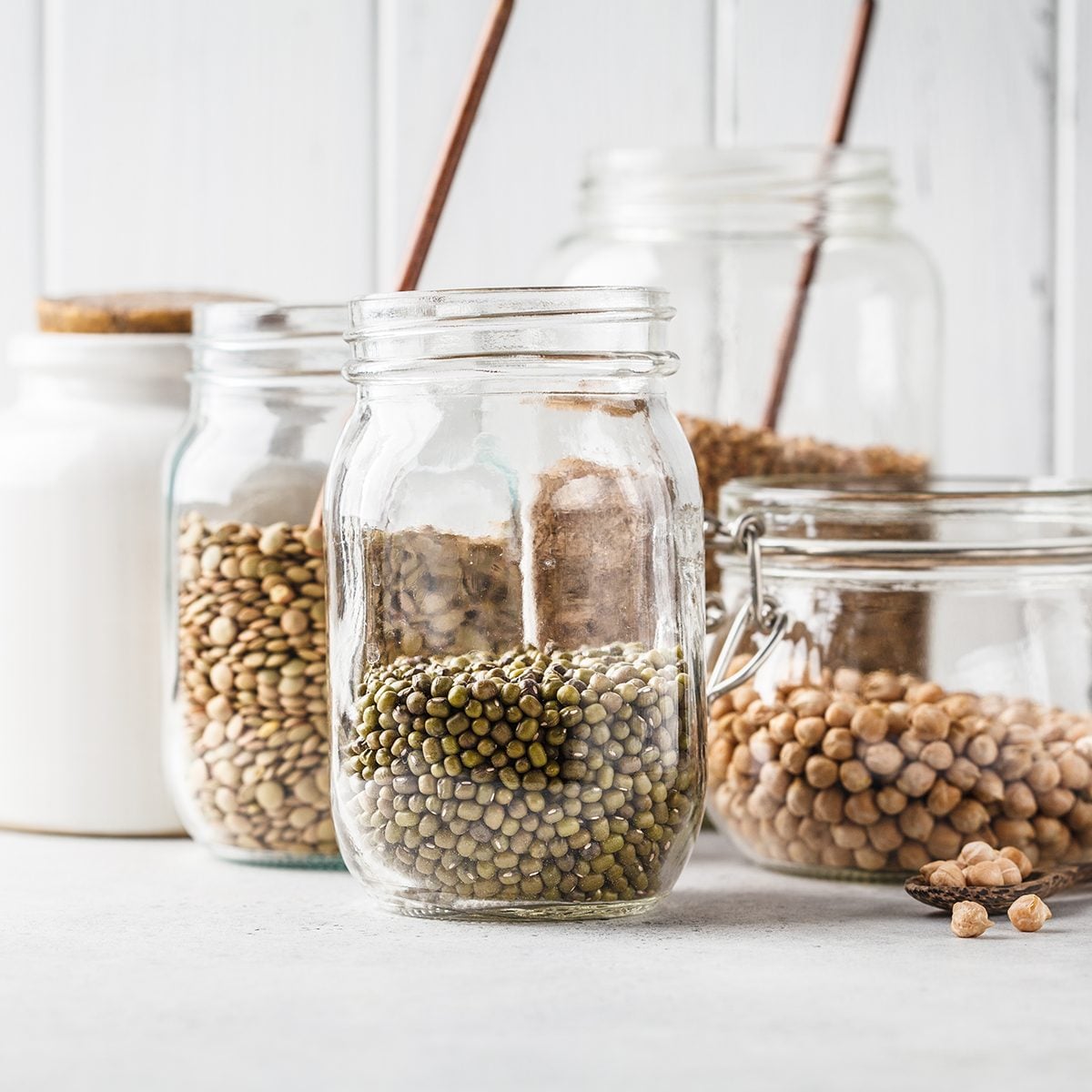 Various legumes: beans, chickpeas, buckwheat, lentils in glass jars on a white background. Healthy vegetarian food, vegetable protein, plant based diet concept.