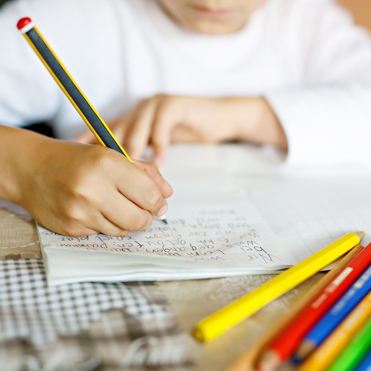 Child doing homework and writing story essay. Elementary or primary school class. Closeup of hands and colorful pencils.