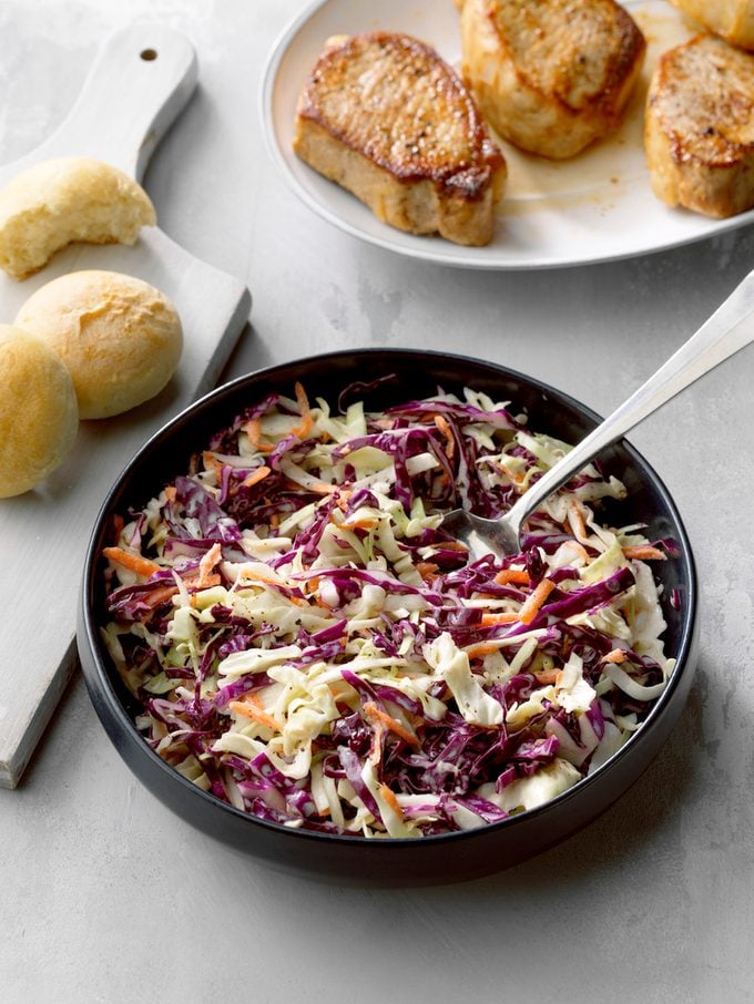 Easy Coleslaw; High slight overhead camera angle; Grey Russian surface; Hard rolls; Pork tenderloins plate filler; dark blue serving bowl; grey painted cutting board