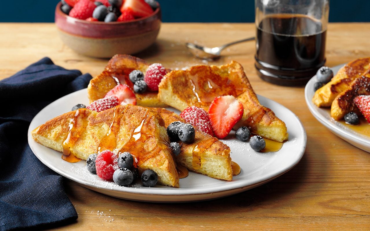 how to make french toast The Best French Toast; half-and-half cream; egg yolks; brown sugar; vanilla extract; ground cinnamon; ground nutmeg; brioche bread; butter; maple syrup; fresh berries; whipped cream; confectioners' sugar; powder sugar; fresh berries; french toast; light wood surface; wood surface; green background; teal background; syrup bottle; syrup; blue cloth; blue background; horizontal