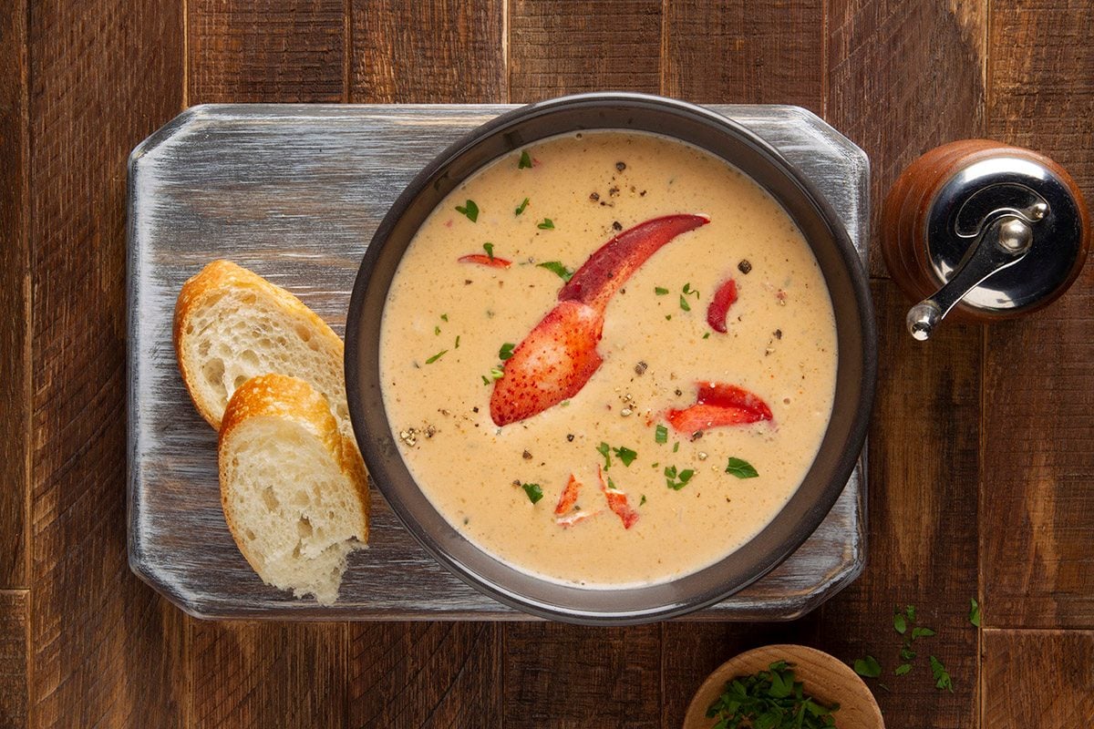 Homemade lobster bisque soup from scratch on table with bread.