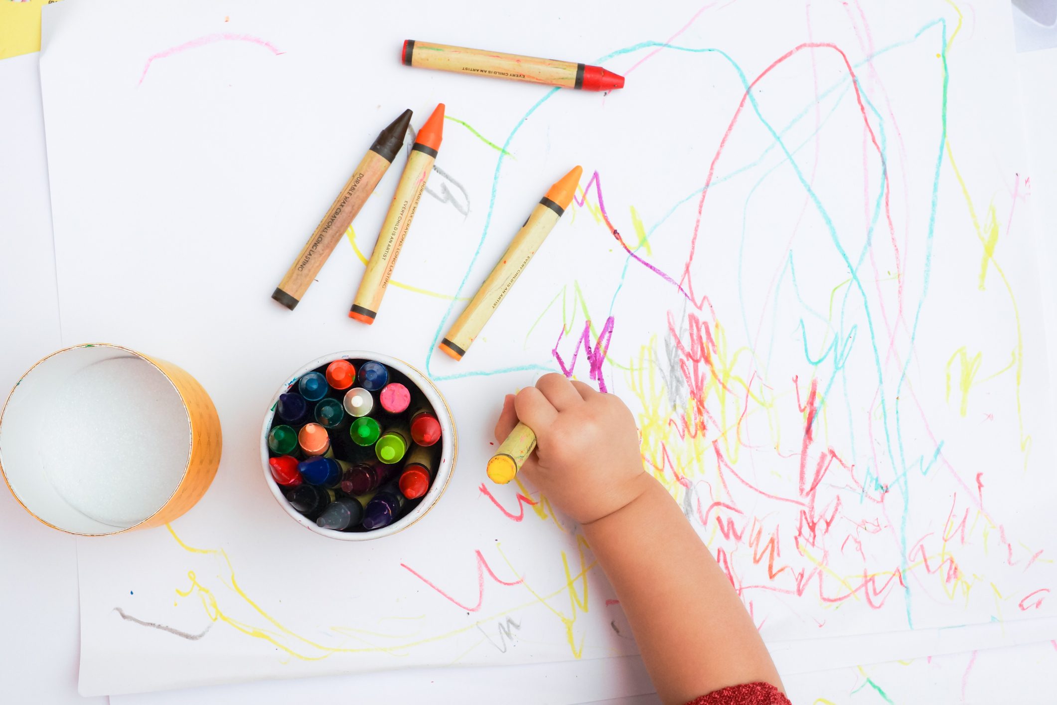 Baby's Hand Drawing On The White Paper With Colorful Crayons