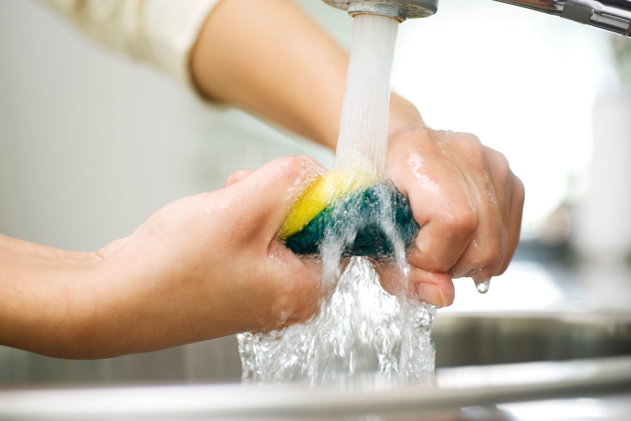 Person rinsing sponge under kitchen faucet