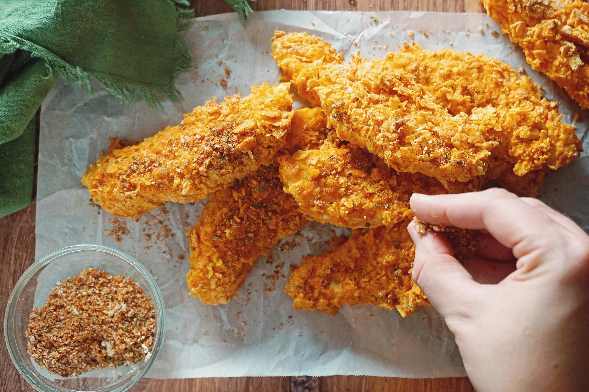 putting spices on Dorito Chicken Tenders after baking