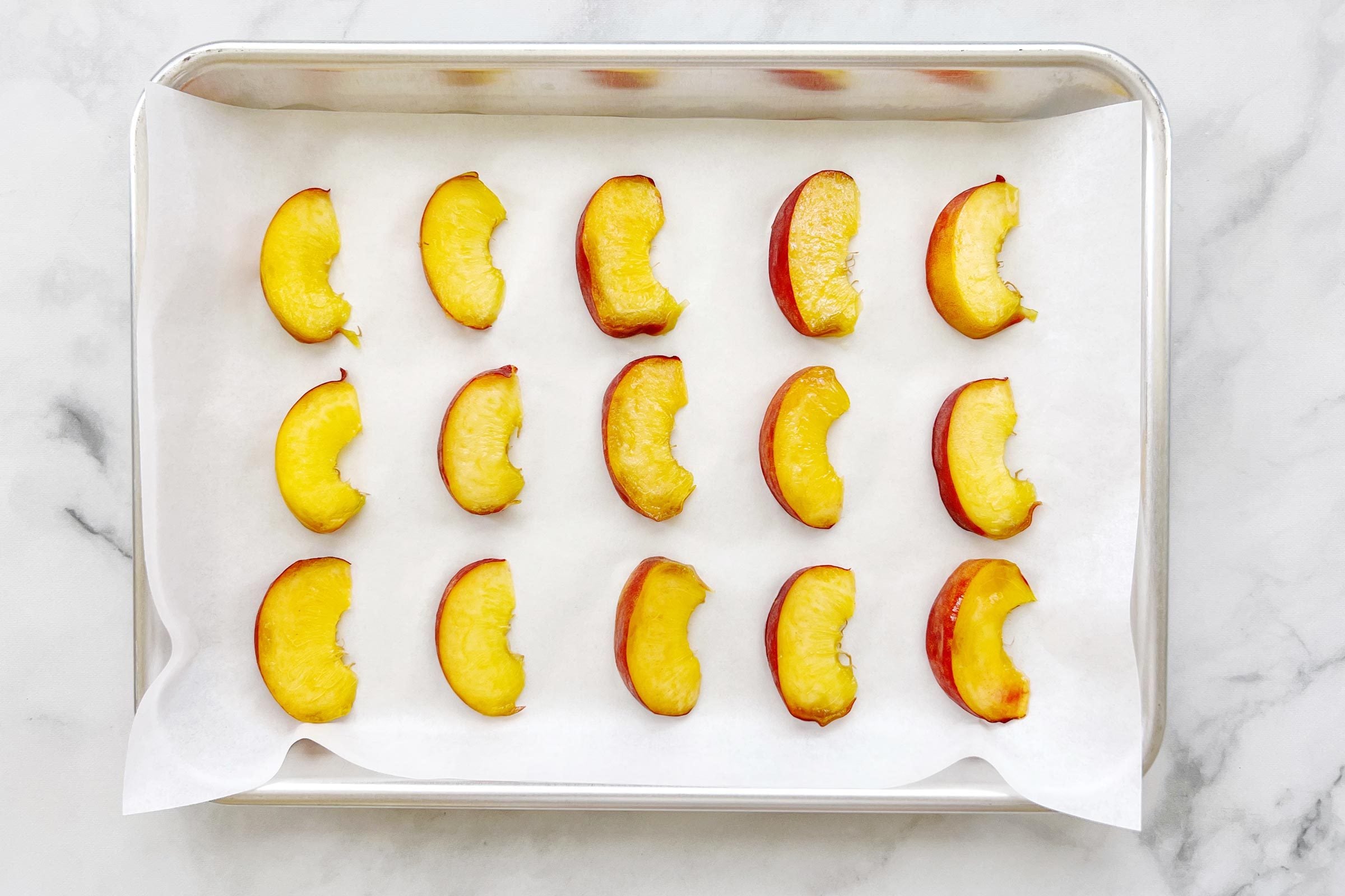 peach slices on a cookie sheet with parchment paper