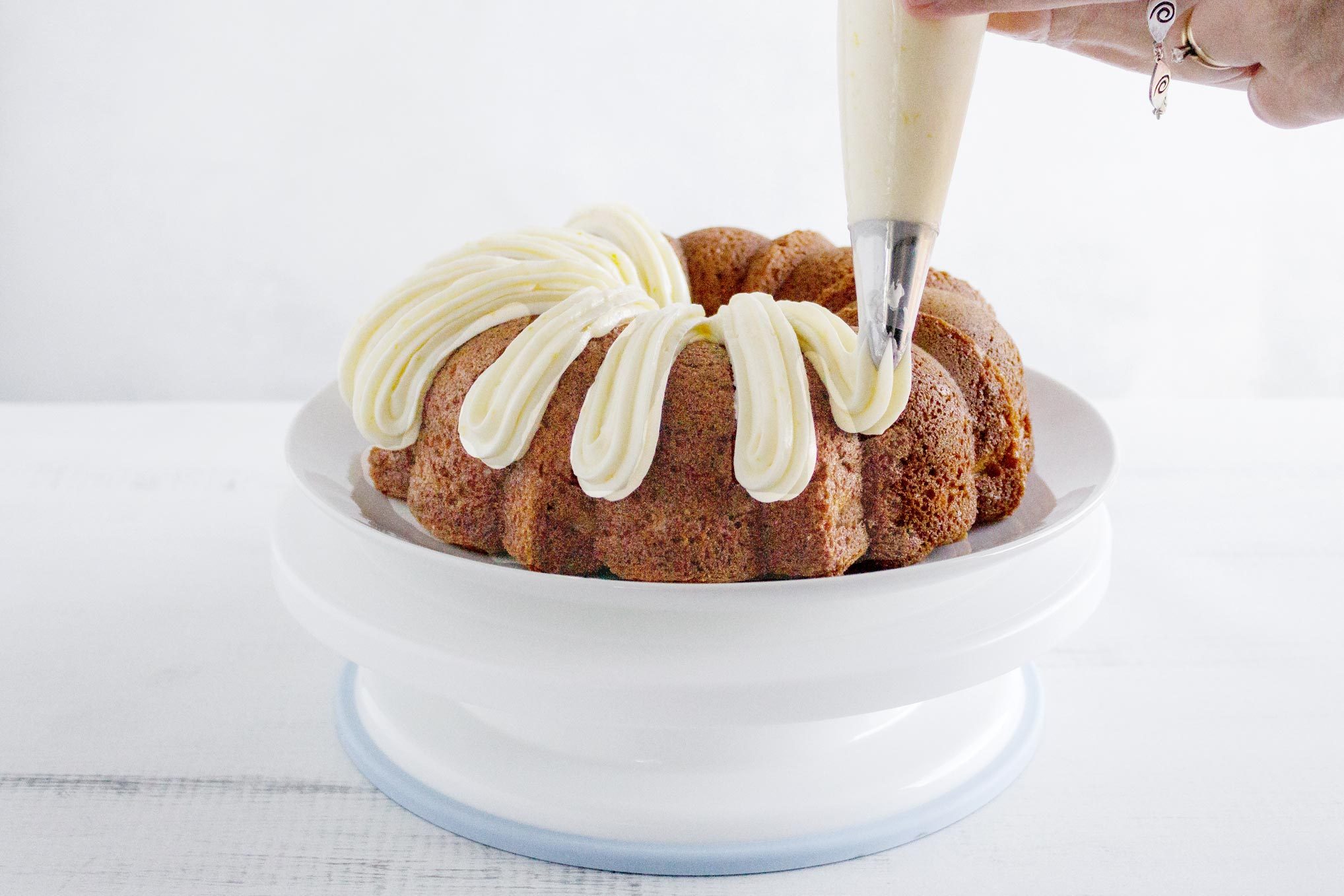 frosting a bundt cake with buttercream frosting in a piping bag