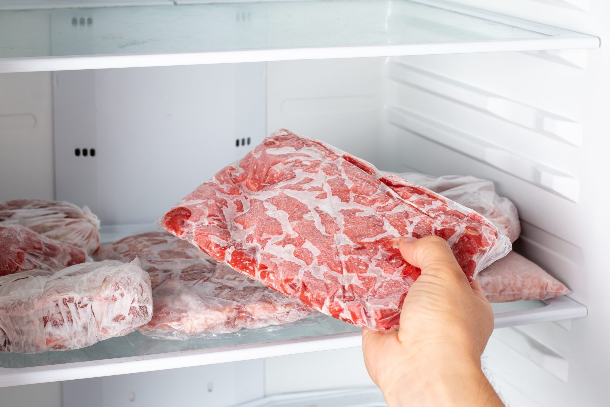 Closeup of hand choosing fresh raw meat in the freezer.