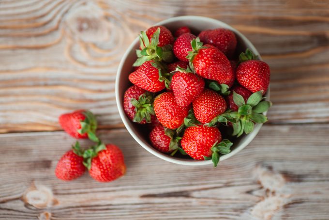 Bowl of ripe strawberries on wooden table - stock photo