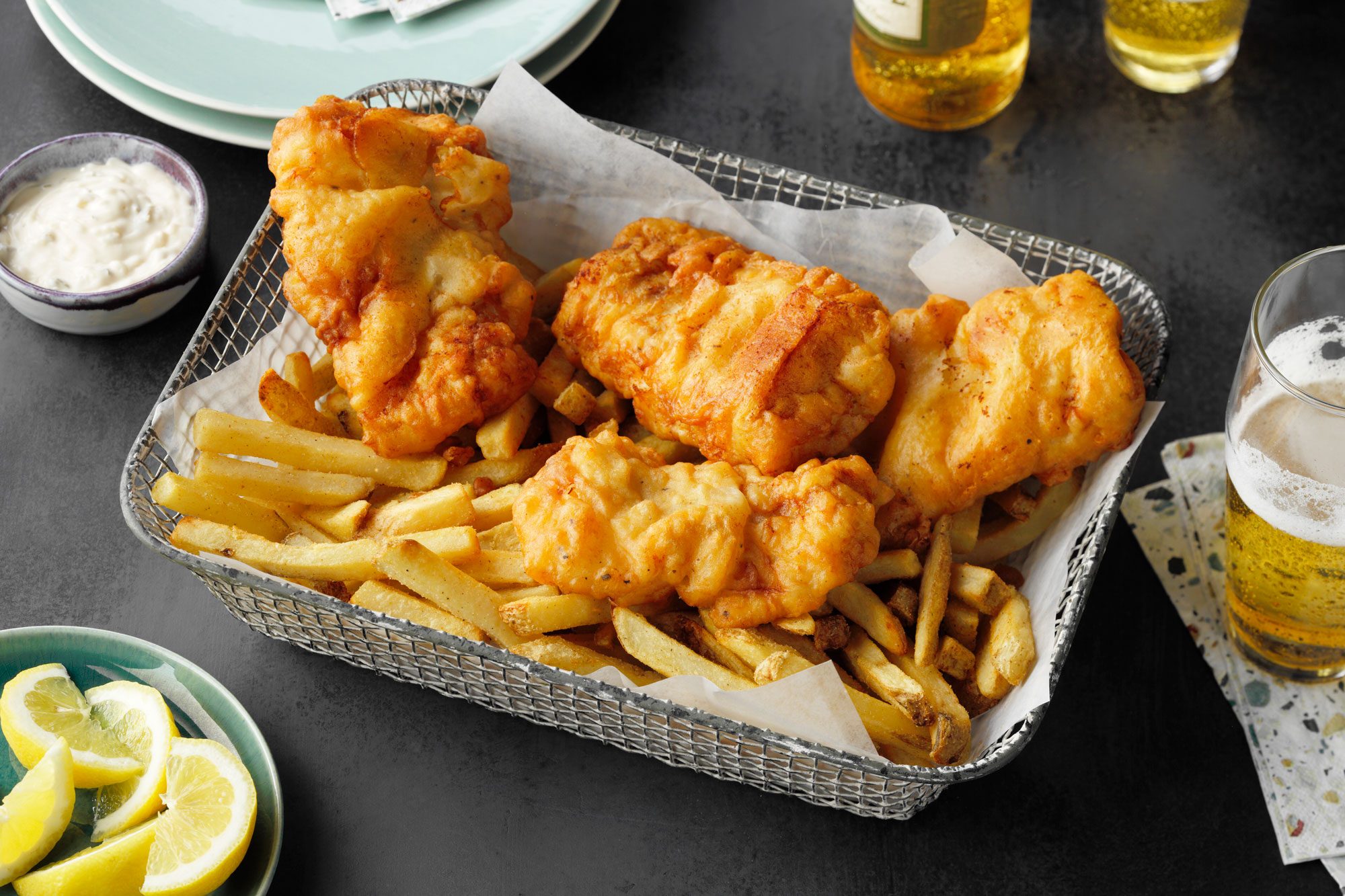 Beer Battered Fish On a Platter with french fries. glasses of beer and serving plates nearby