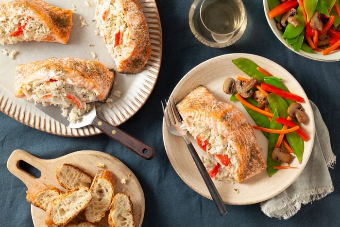 stuffed salmon on a plate with a side of mixed veggies and a serving platter with more stuffed salmon off to the side