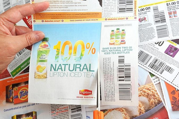 Woman Cuts Coupons from advertisement section of the Sunday Newspaper with bright orange scissors