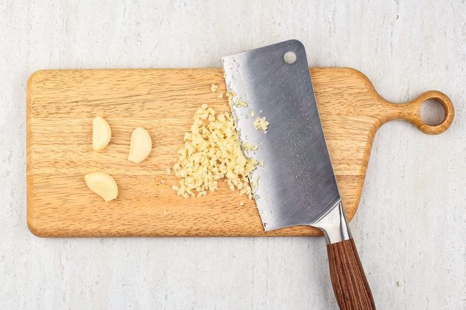 Chopped Garlic On The Wooden Chopping Board With Chopper Knife