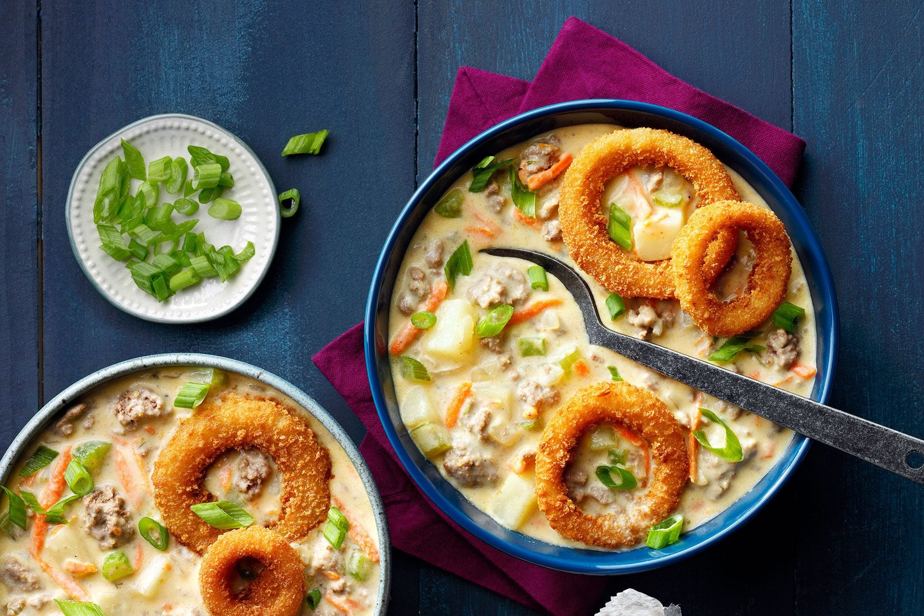 Cheeseburger Soup served with onion rungs in it on blue wooden surface