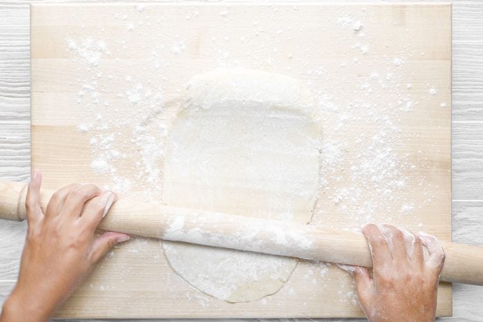A person rolling the dough ightly floured surface