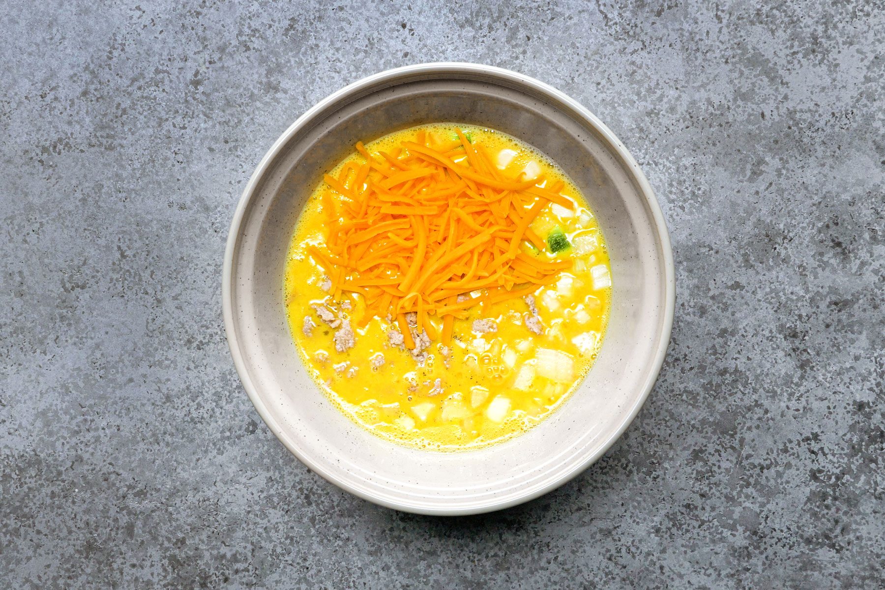 Eggs and cheese mixed in a large bowl, placed on a marble surface.