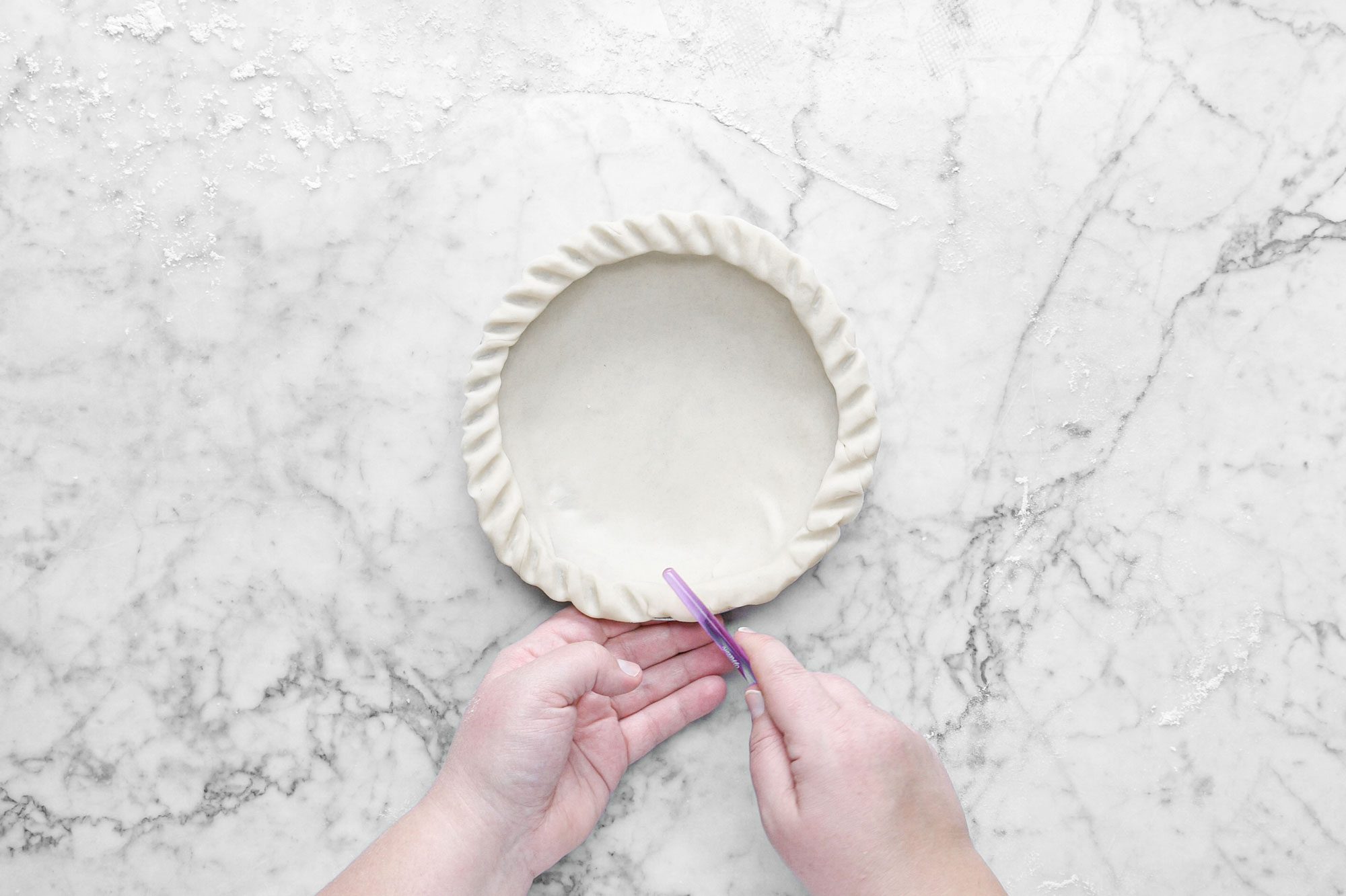 a person's hands flute the edges of pie crust