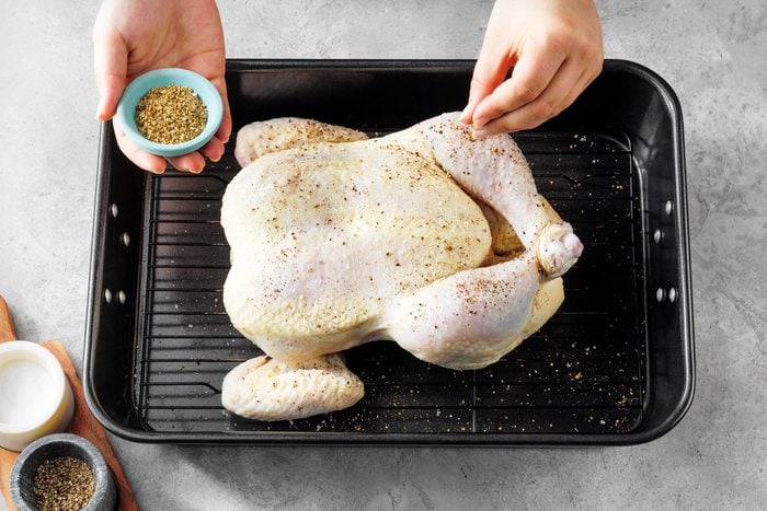 Sprinkling Oregano over chicken placed in a roasting pan on marble surface