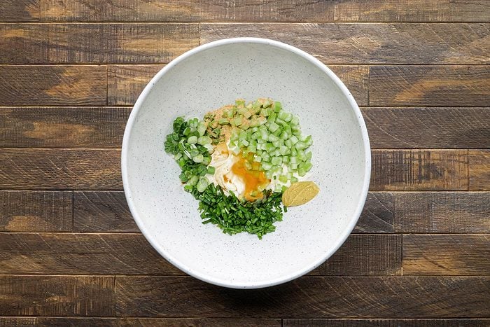 Mixing together mayonnaise, celery, green onions, chives in a large bowl.