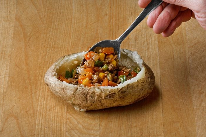 Adding meat mixture into each potato shell with a spoon