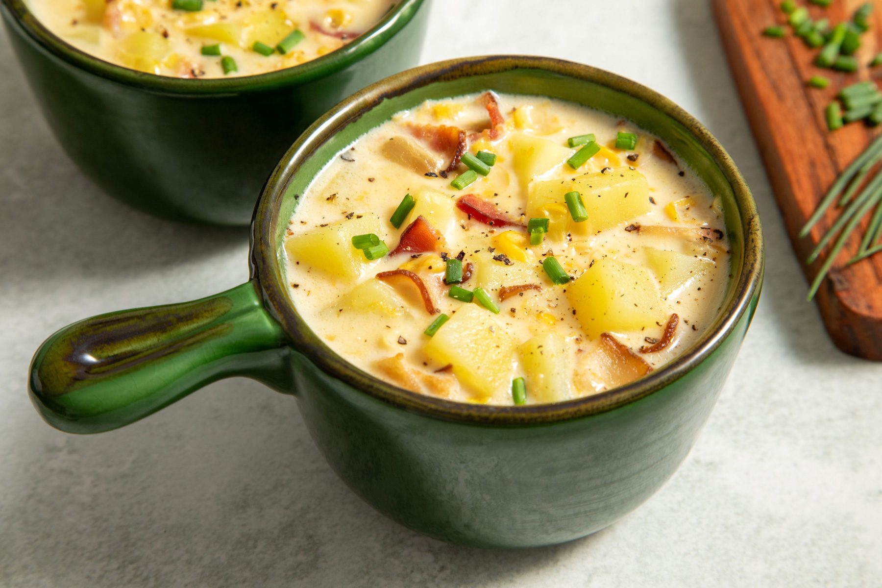 A close-up of two green bowls filled with corn chowder with bacon soup